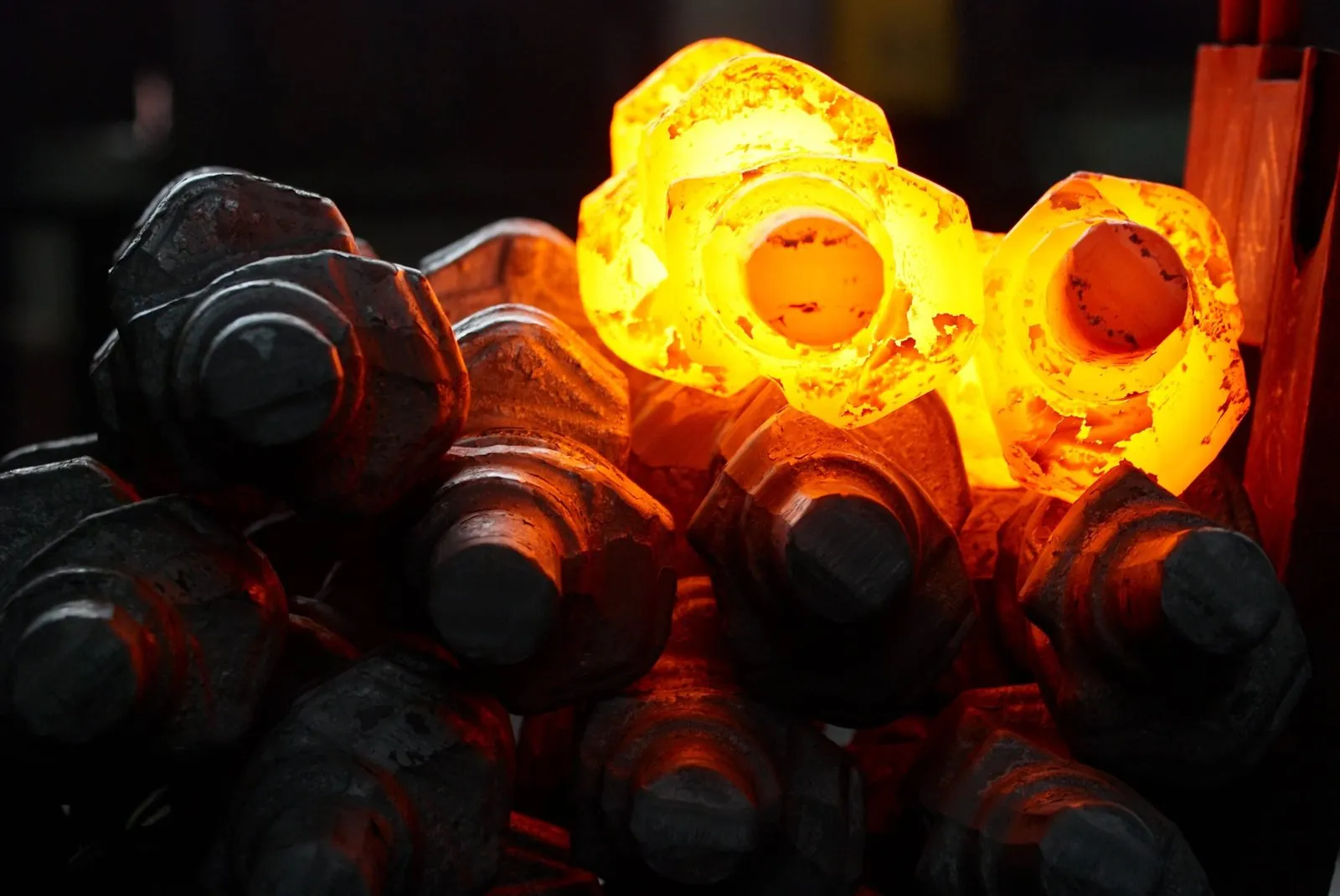 Hot-forged bolt heads glowing orange after forging
