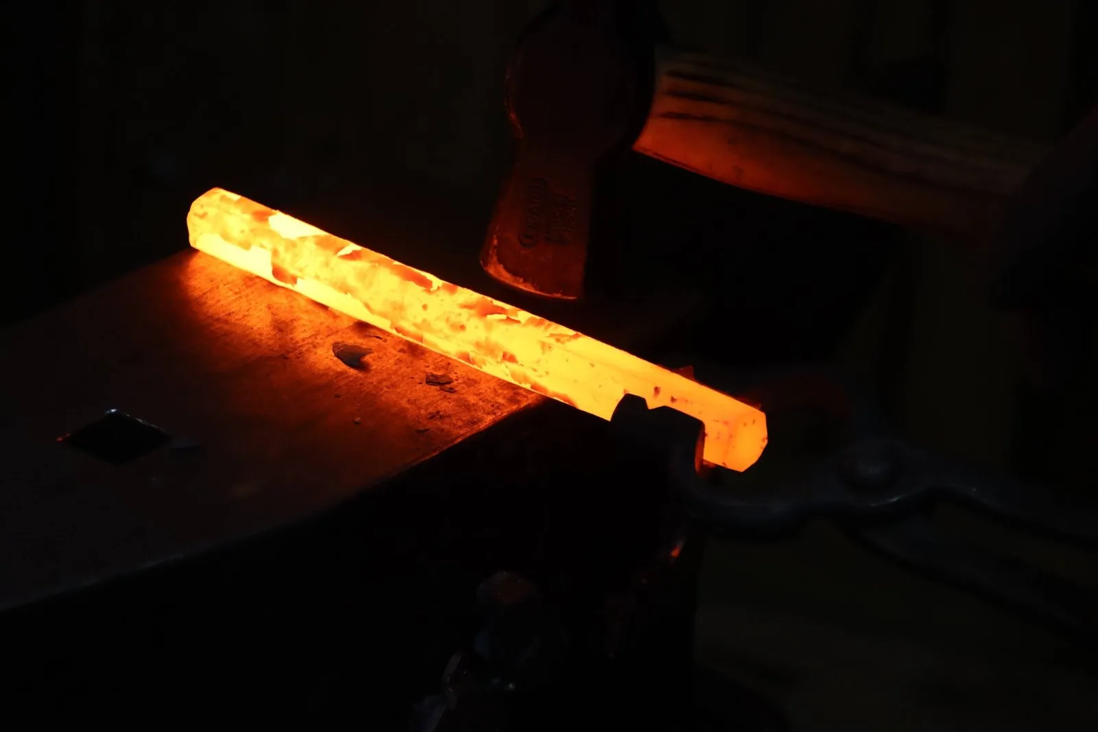 A glowing forged bar under a forging hammer